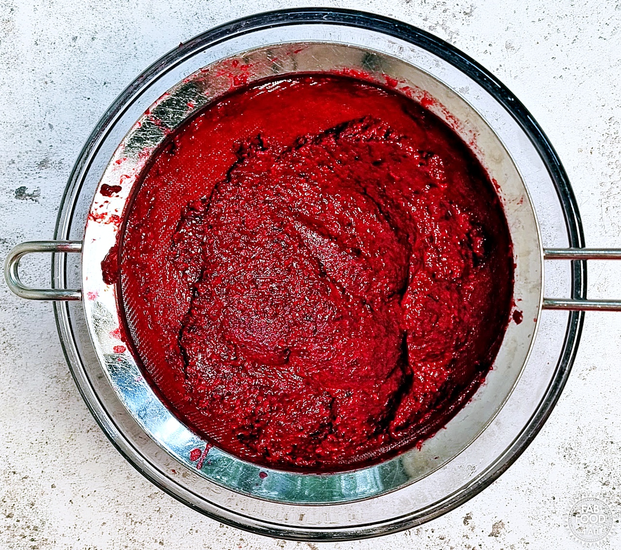 Blackberry and raspberry seeds/pulp left in the sieve over a glass bowl.
