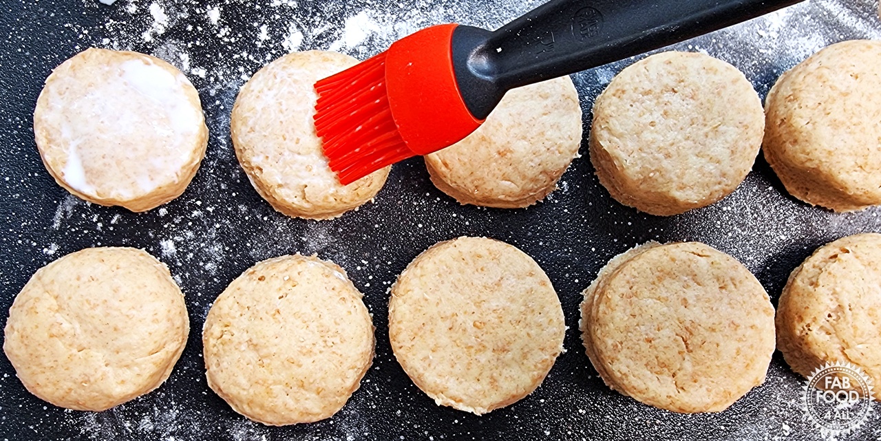 Full-fat milk being painted onto the spelt scone tops with a silicone pastry brush.