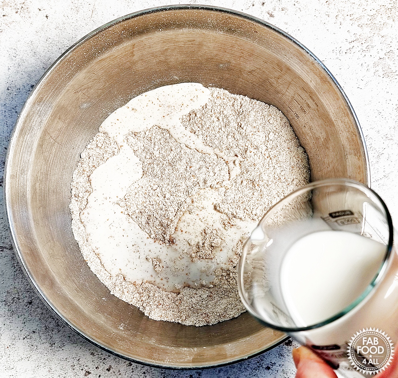 Full-fat milk being poured into flour, baking powder and butter mixture that now resembles breadcrumbs.