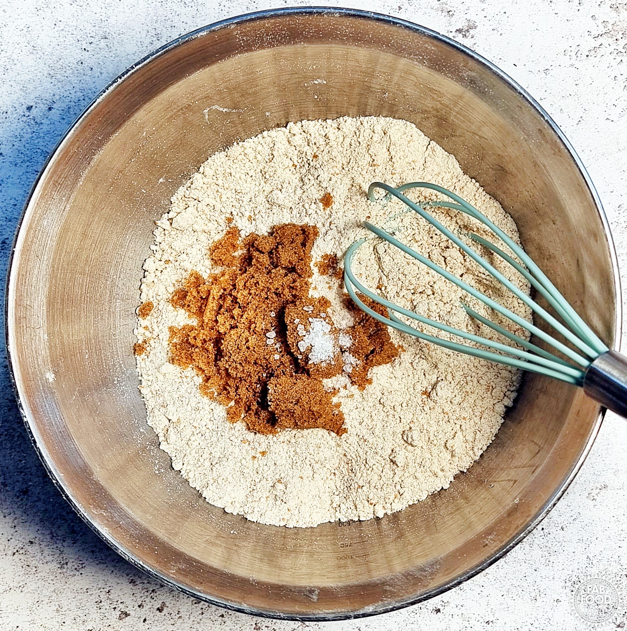 Light soft brown sugar and salt being stirred into flour mixture with a whisk.