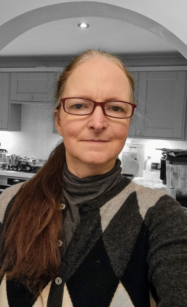 Upper body shot of me (Camilla Hawkins) standing under an archway in the kitchen with units in the background.