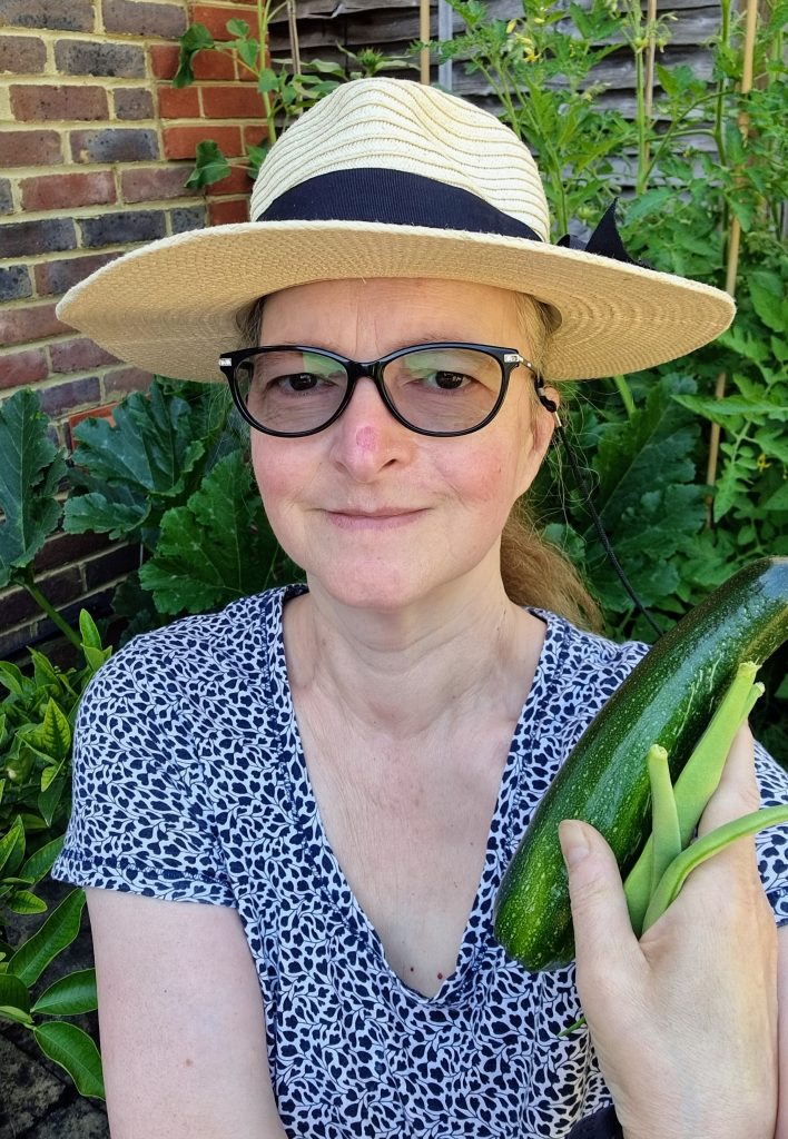 Camilla Hawkins (me) with homegrown courgette and French beans in one hand in front of my raised bed.