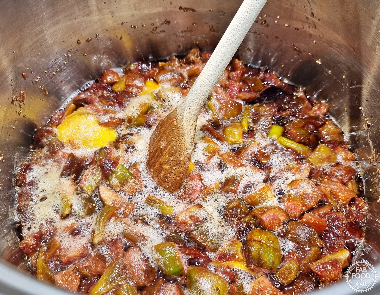 Fig Jam mixture simmering in a large stainless steel pan whilst being stirred with a wooden spoon.