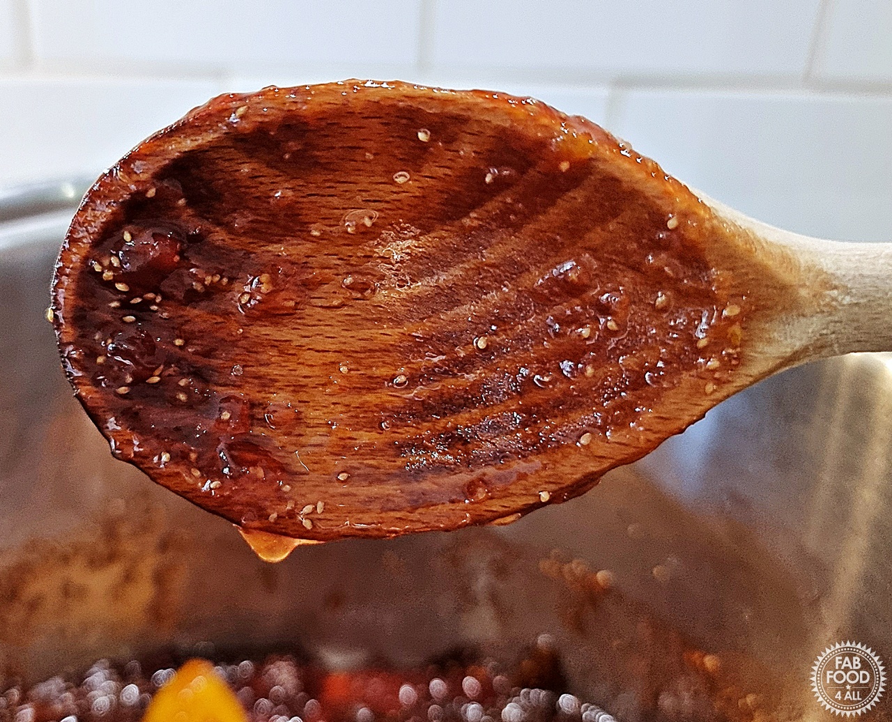 Drip test showing the last drop of jam hanging from the side of a wooden spoon.