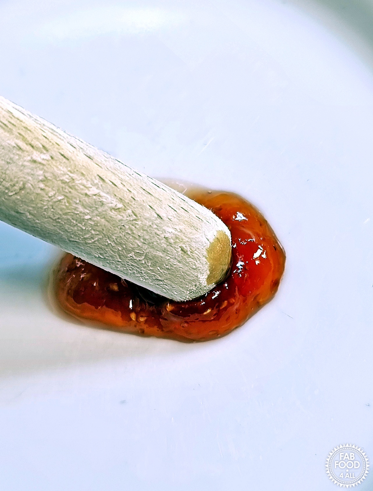 Blob of fig jam being pushed with a wooden spoon handle showing gentle wrinkle for chilled plate test.