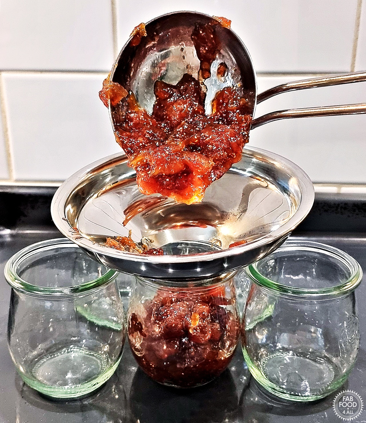 Fig Jam being ladled into glass jars using a jam funnel.