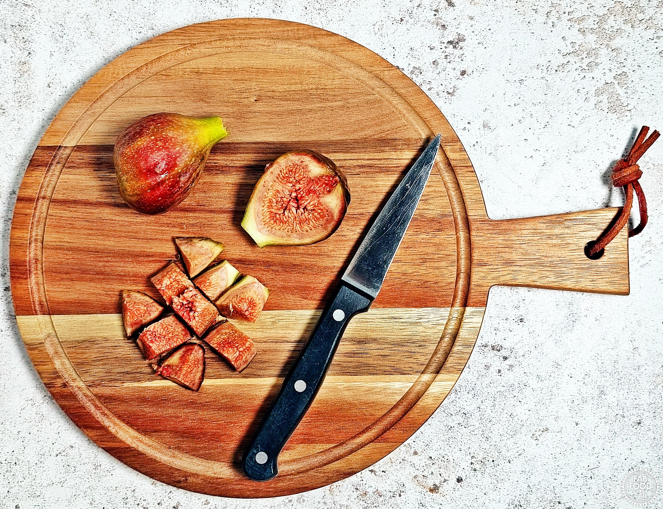 2 figs on a chopping board with knife, 1 cut in half and the other half cut into 9 pieces.