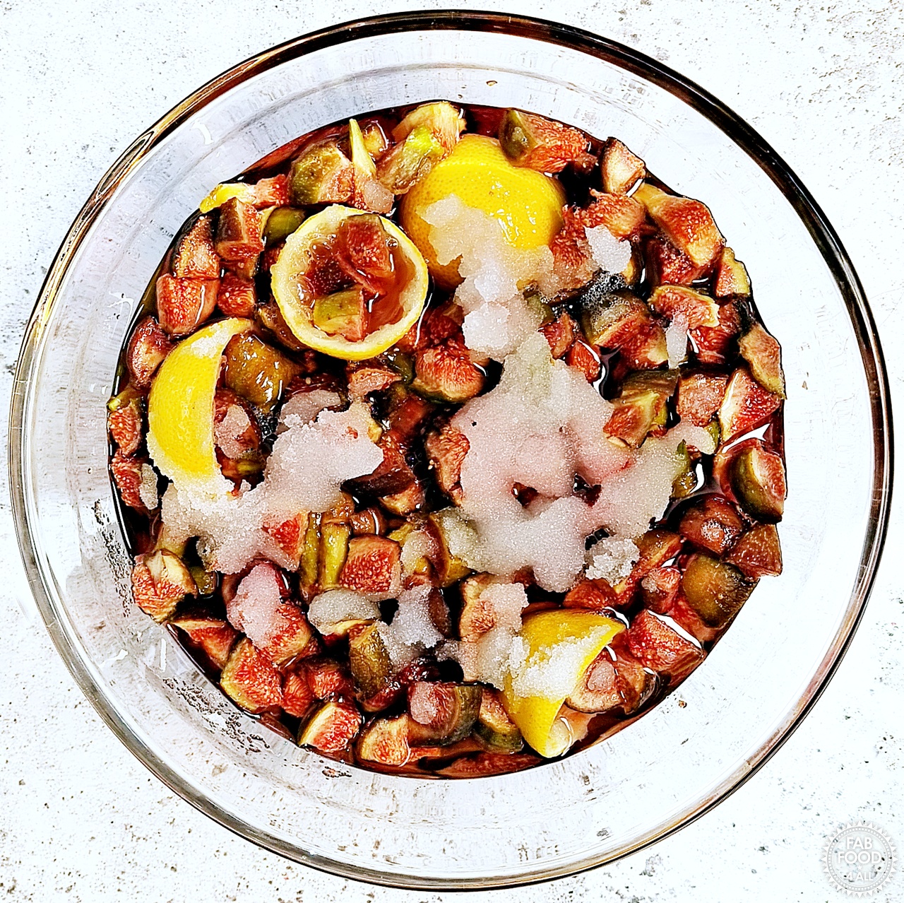 Chopped figs, lemon rinds, granulated sugar and lemon juice in a glass bowl after macerating overnight. Sugar has mostly dissolved.
