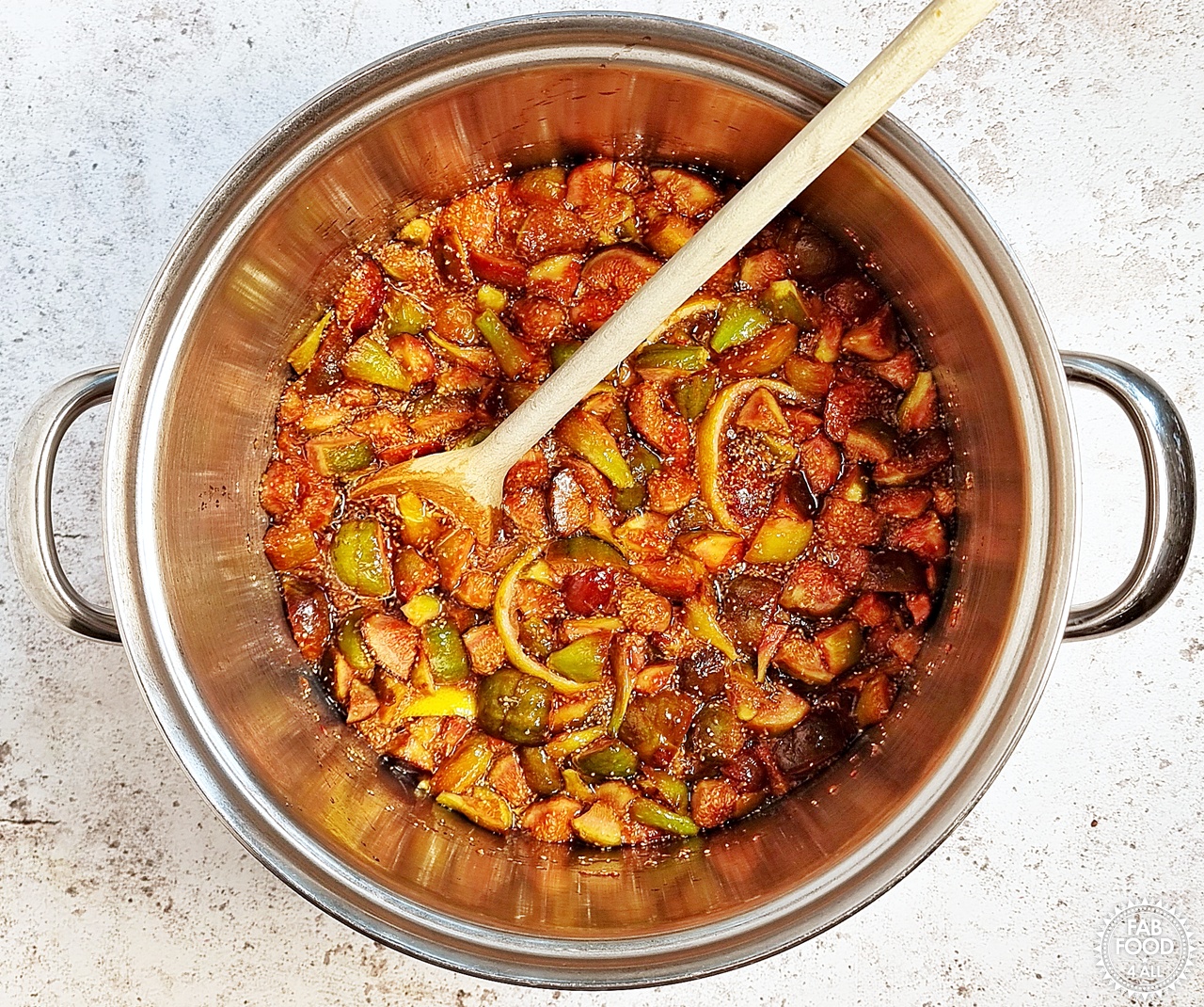 Macerated fig mixture in a large stainless steel pan with wooden spoon having been gently heated to allow the rest of the sugar to dissolve.