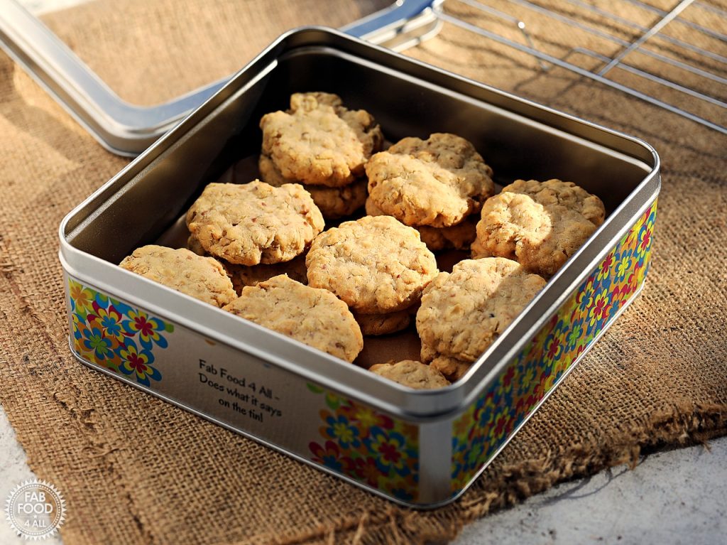 Savoury Spelt Cookies with Cheddar & Peanut Butter in a square cake tin with lid and wire rack in the background on a piece of folded hessian cloth.