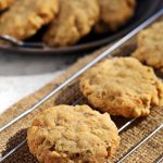 Close up of Savoury Spelt Cookies with Cheddar & Peanut Butter on a wire rack with metal dish of cookies visible in the background.