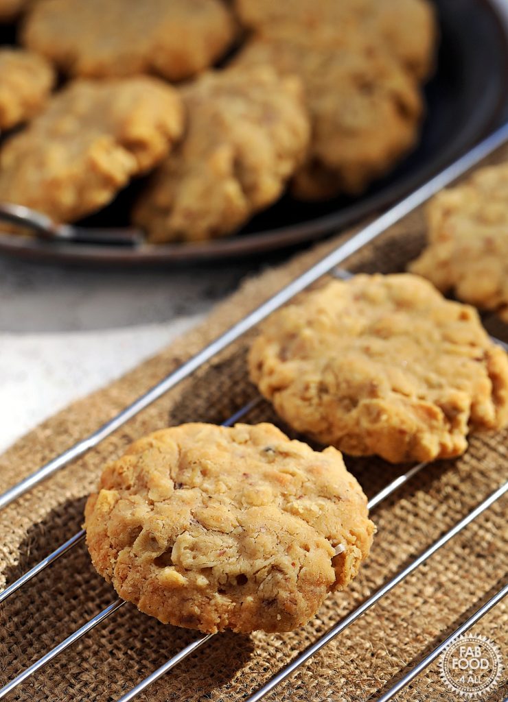 Close up of Savoury Spelt Cookies with Cheddar & Peanut Butter on a wire rack with metal dish of cookies visible in the background.