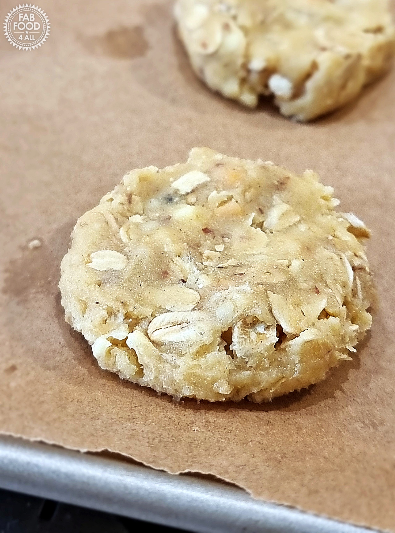 Close up of a raw Savoury Spelt Cookie with Cheddar & Peanut Butter dough on baking paper on a baking sheet; another just visible.